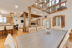 A spacious dining area with a large table, wooden beams, and a high ceiling with a chandelier.