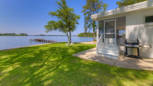 Eine Blockhütte am Seeufer mit verdeckter Veranda, Grill und einer Anlegestelle im Wasser.