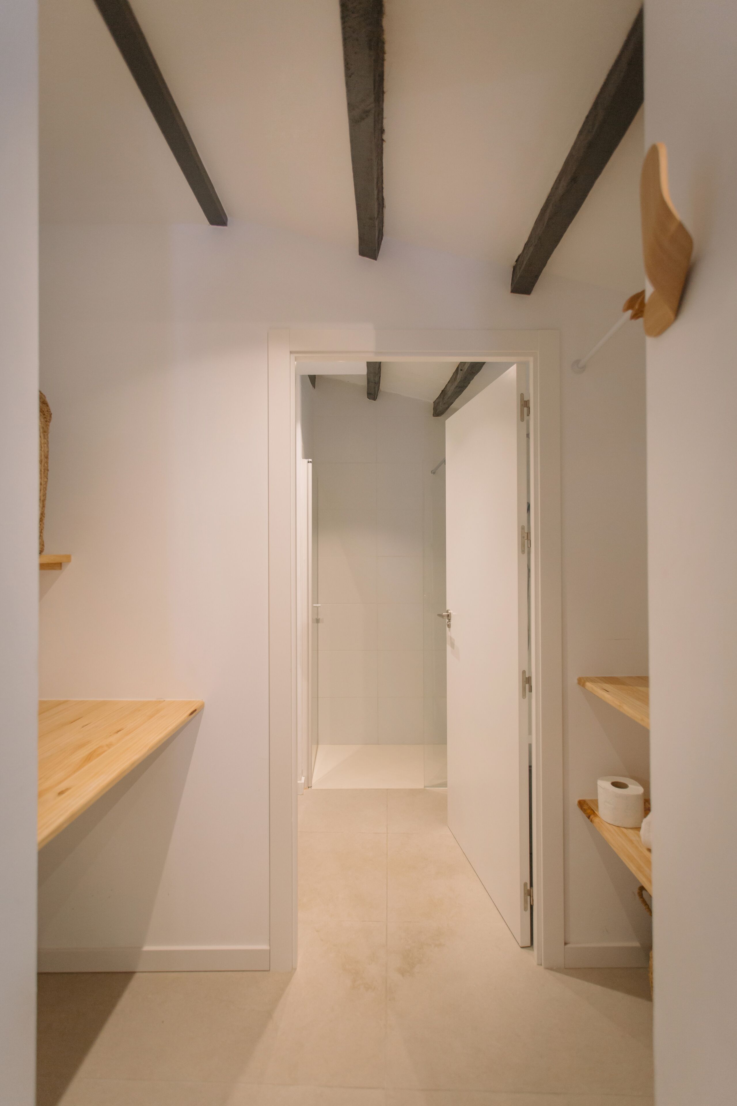 A narrow hallway with a wooden shelf on the left and a white door at the end.