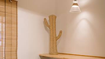 A room with a wooden ceiling, a woven chair, a table with stools, a cactus sculpture, and a hanging light fixture.