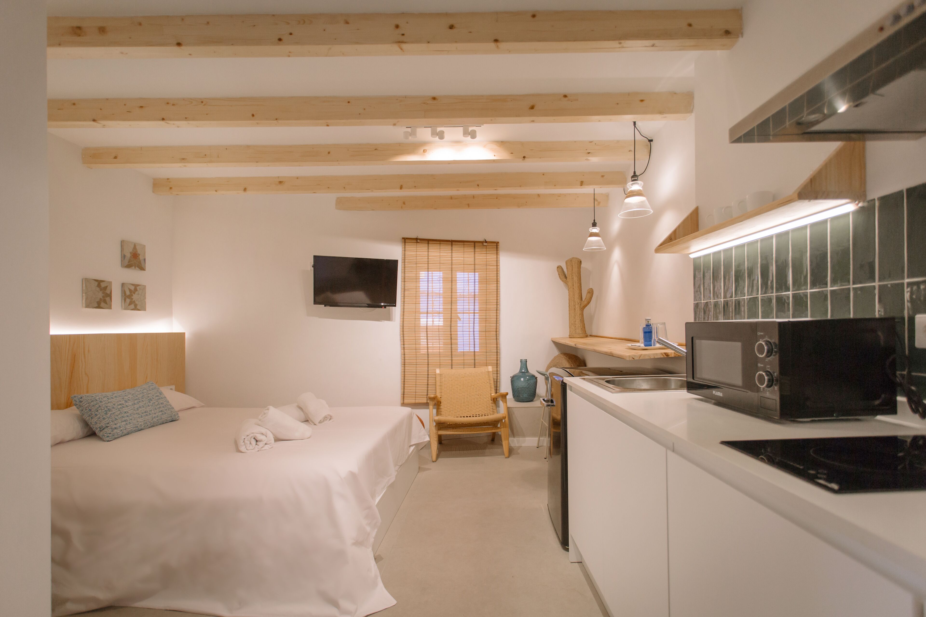 A compact hotel room with a bed, a small desk, a microwave, and a TV.