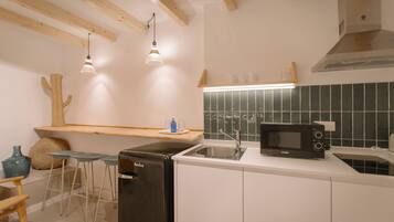 Una cocina compacta con armarios blancos, un refrigerador negro, un microondas y una barra de madera con taburetes.