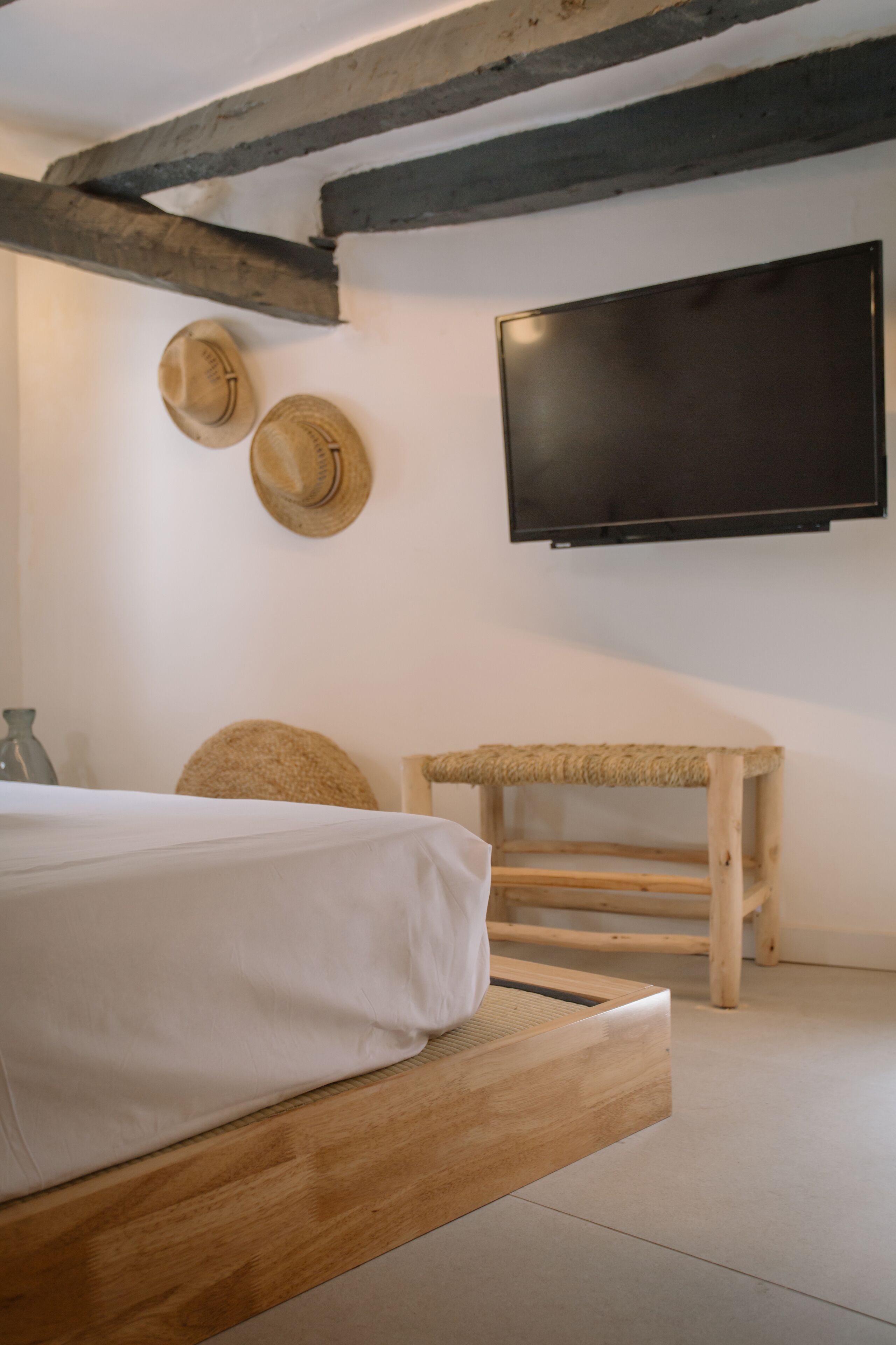 A bedroom with a wooden bed, a television mounted on the wall, and two hats hanging on the wall.