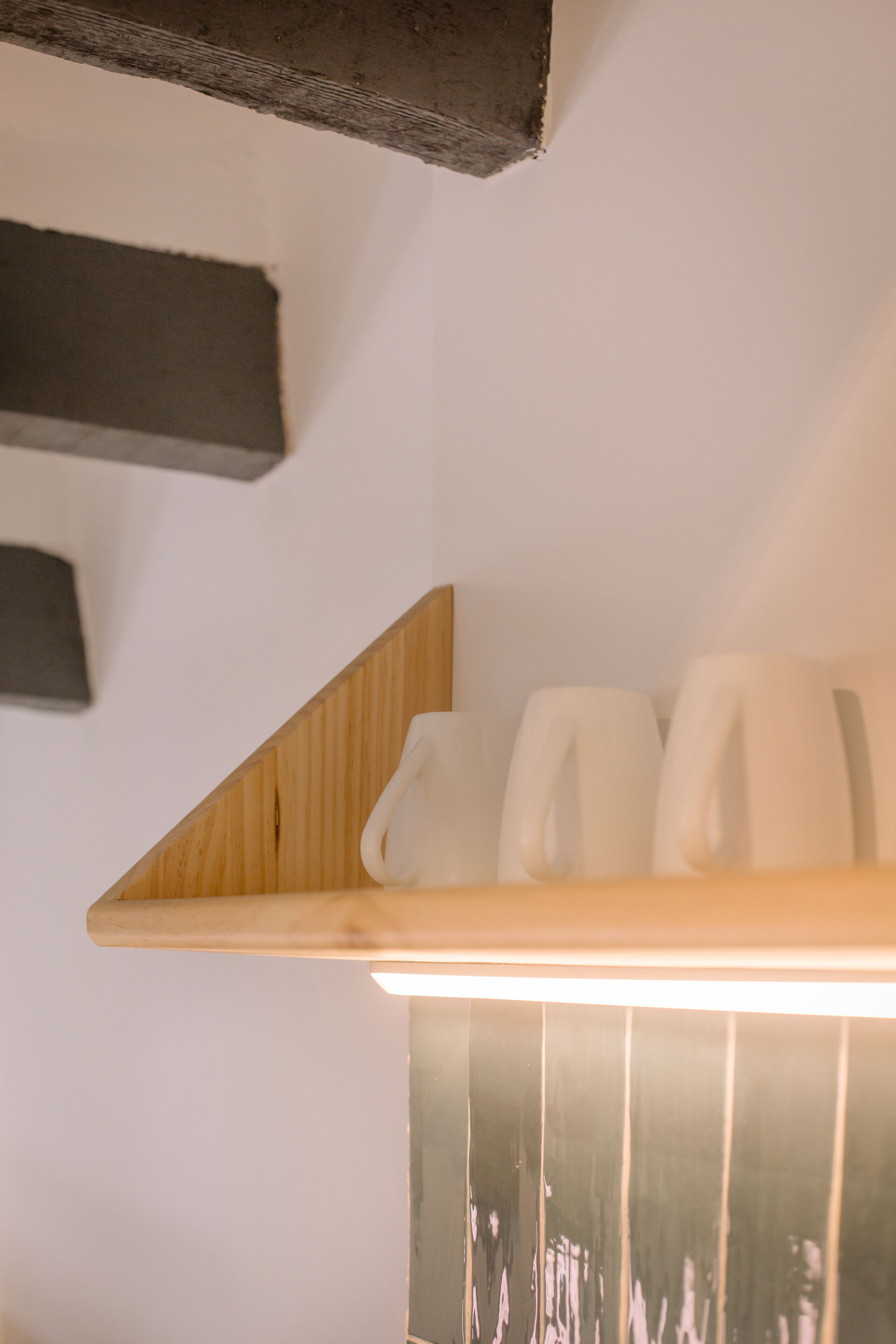 A wooden shelf with three white mugs against a white wall.