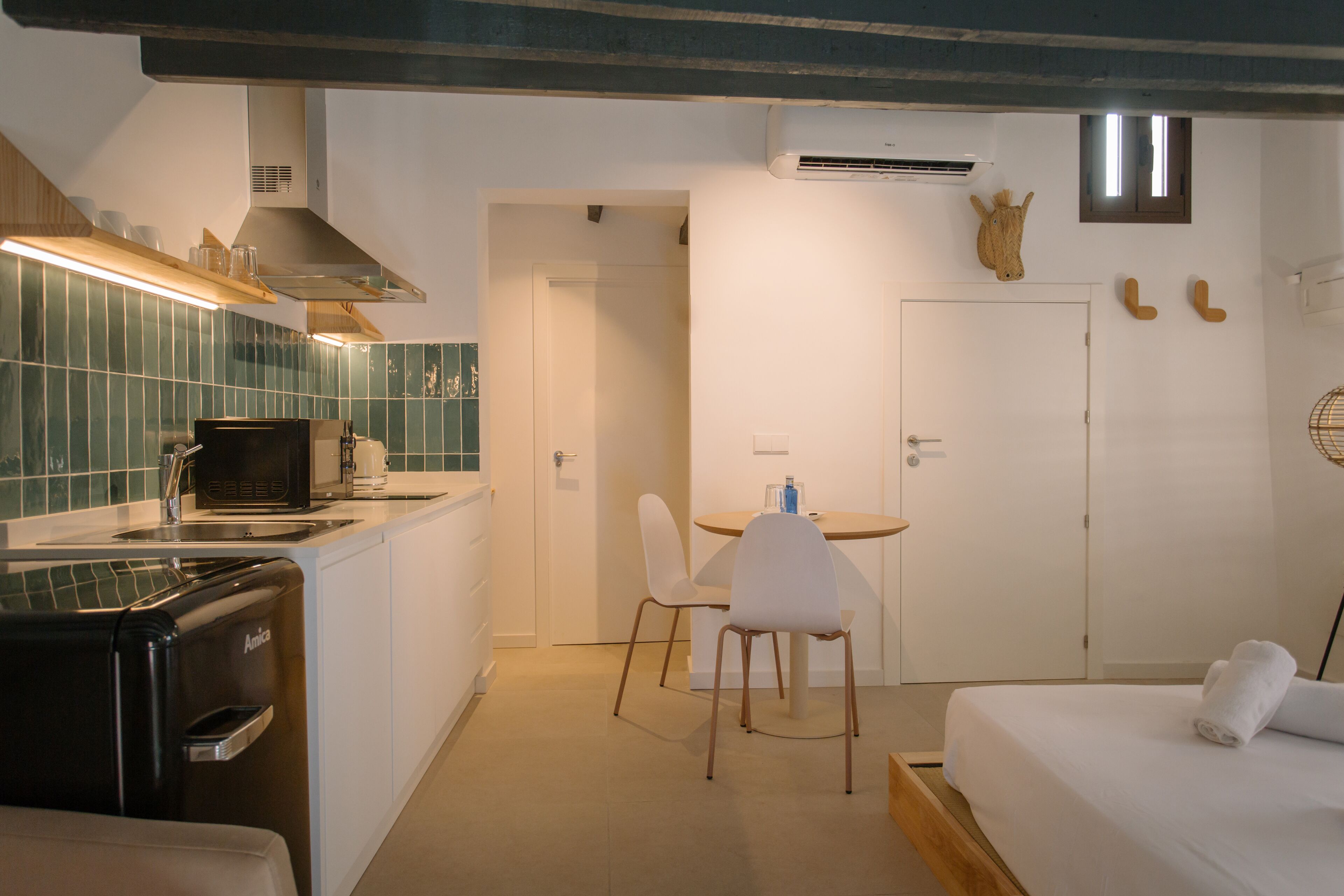 A compact hotel room with a kitchenette, a dining area, and a bed.