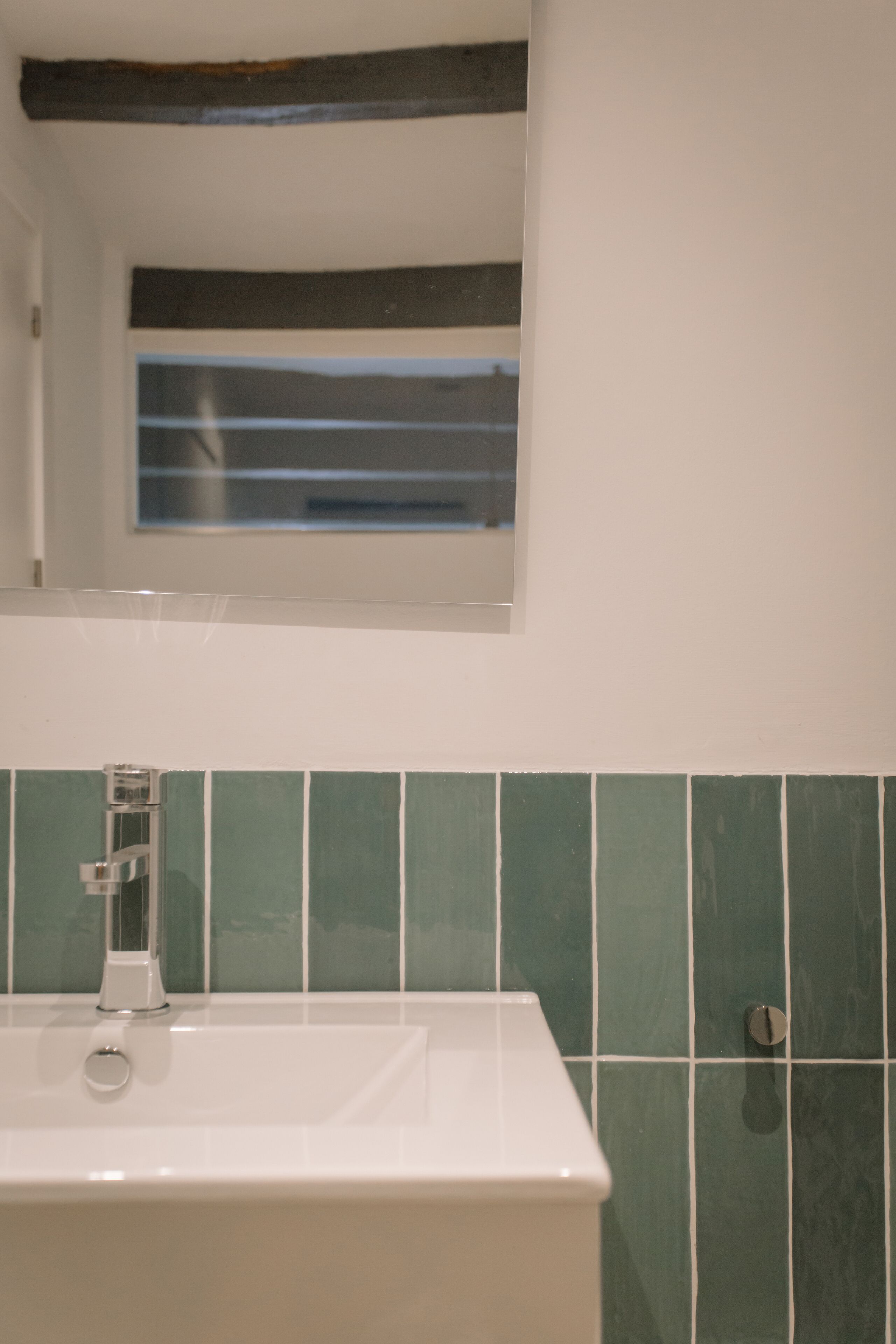 A bathroom with a white sink, green tiled walls, and a window above the mirror.