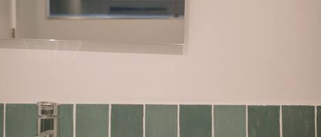 A bathroom with a white sink, green tiled walls, and a window above the mirror.