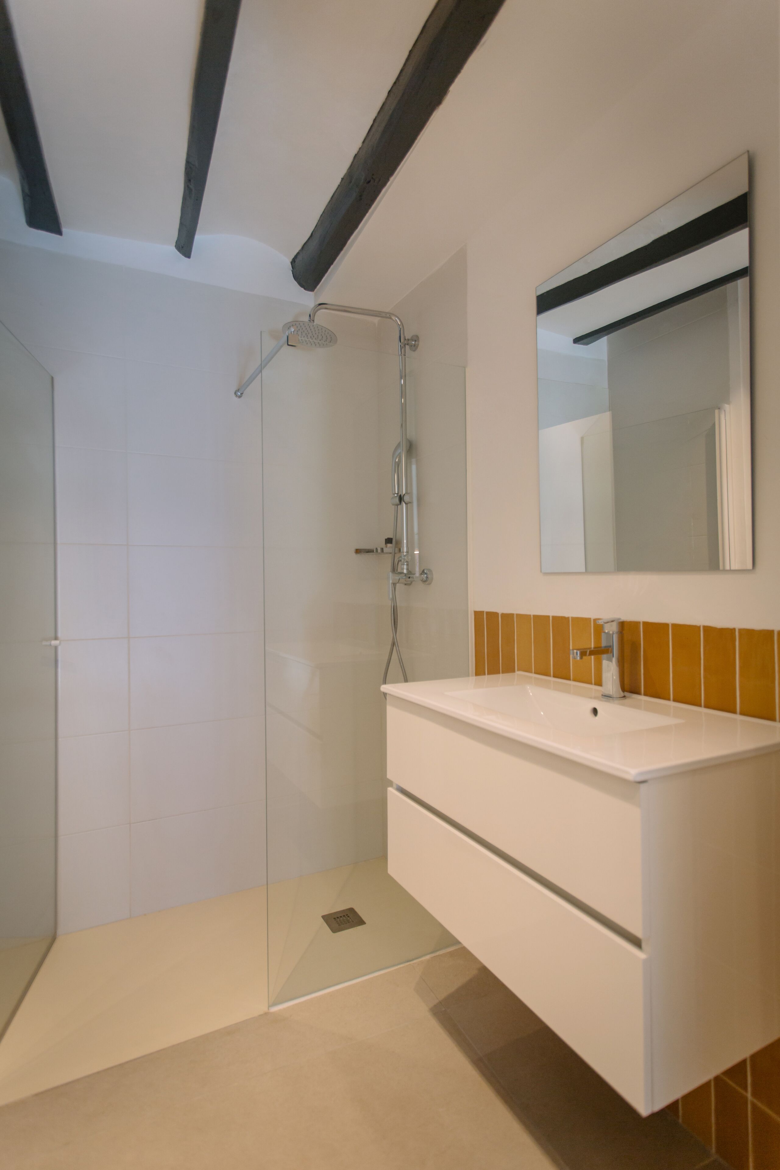A modern bathroom with a glass-enclosed shower, a white vanity with a mirror, and a tiled floor.