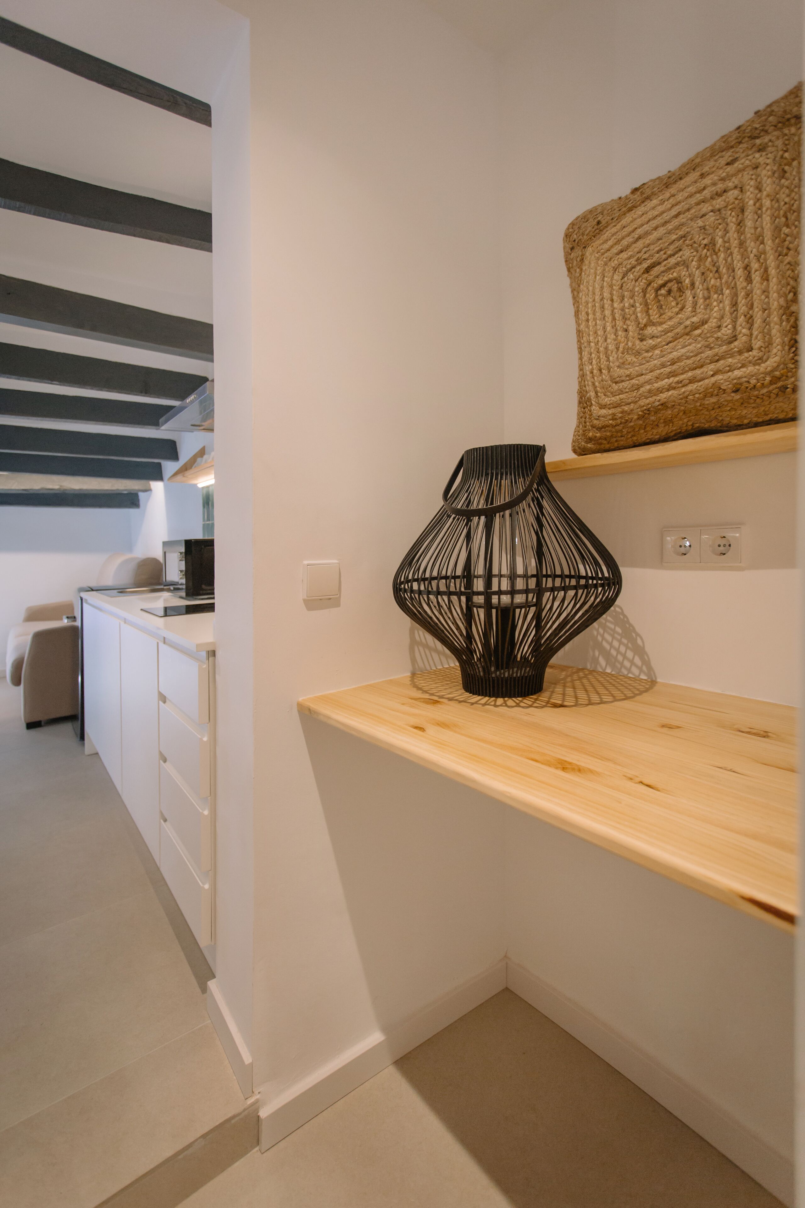 A modern kitchen with white cabinetry, a wooden countertop, and a black woven vase on the shelf.
