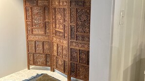 Ein Zimmer mit einem dekorativen Holzverpartition, einem gemusterten Teppich und einem kleinen Hocker.
