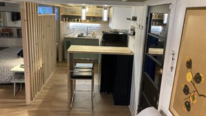Eine kompakte Küche mit Kochinsel, ein Essbereich mit einem Stuhl und ein Bett im Vordergrund.