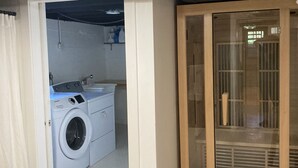 Ein Waschraum mit Waschmaschine und Trockner, eine Glastür, die auf einen Balkon führt, und eine Decke mit einer runden Leuchte.