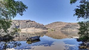 A calm lake with a boat docked on the shore, surrounded by rocky terrain and sparse vegetation. - RV space on the River Unit B -minutes from Gorge concerts (Quincy)