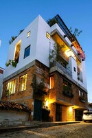 Un edificio de varios pisos con una combinación de ladrillo y paredes blancas, ventanas amplias y balcones con plantas.
