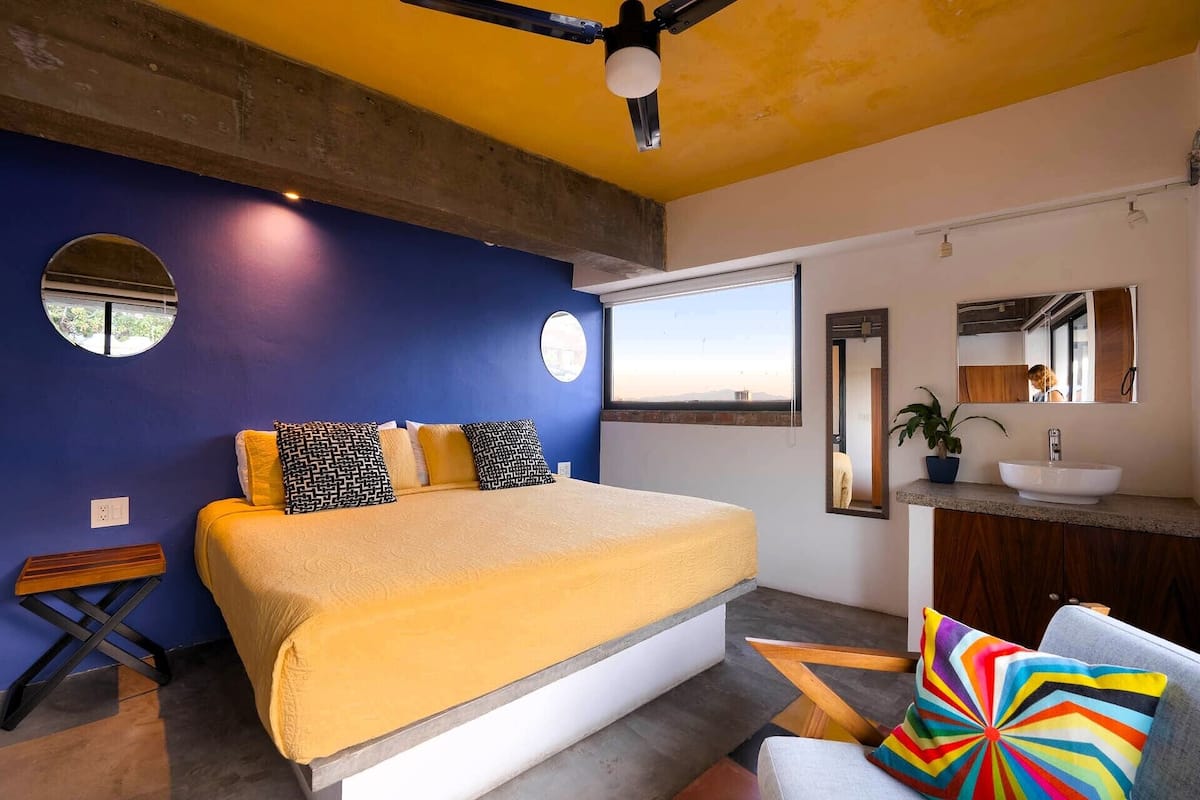 A modern bedroom with a large bed, a bathroom with a sink and mirror, and a view of the outdoors.