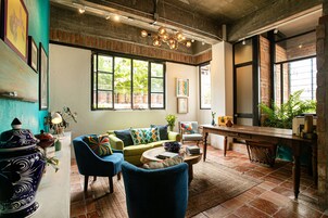 Una sala de estar acogedora con sofá, sillones, una mesita de centro y una mesa de comedor. Amplias ventanas ofrecen vistas a zonas verdes exteriores.