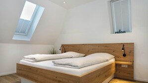 A modern bedroom with a wooden bed, skylight, and a wall-mounted shelf. - The approx. 45 m² large and very chic 2-room apartment for 1 to 2 persons is located on the Klosterhof Aue in Bad Zwischenahn. (Bad Zwischenahn)