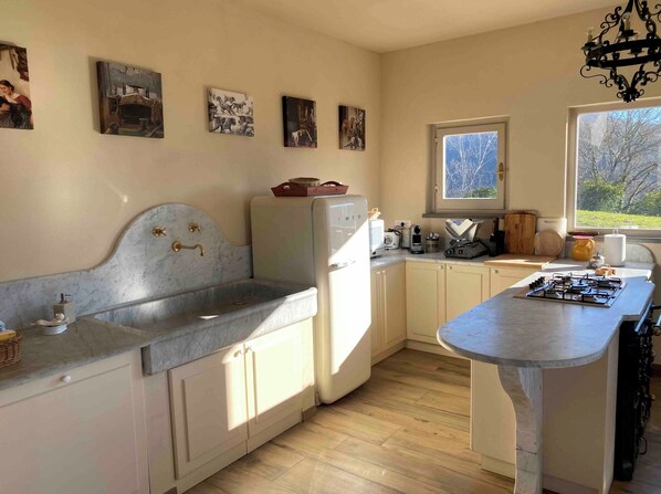 Une cuisine dotée d’un plan de travail en marbre, de meubles blancs, d’une cuisinière encastrée et d’une fenêtre laissant entrer la lumière naturelle.