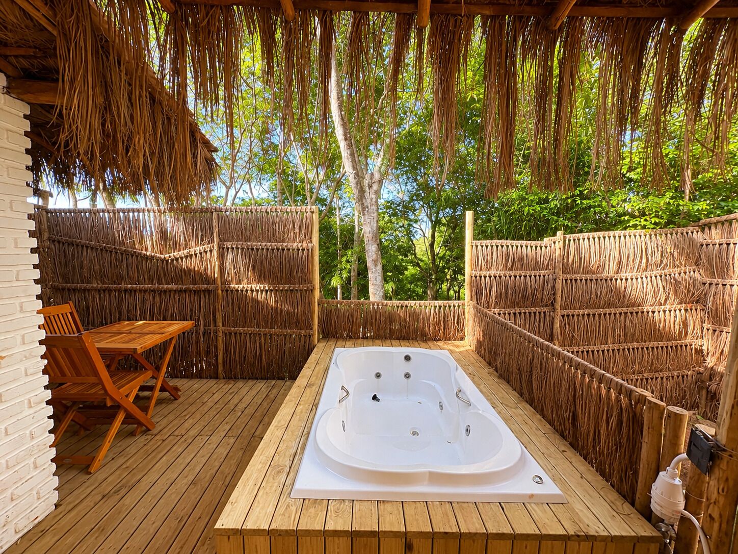 An outdoor hot tub area with wooden flooring, a seating area with chairs, and a thatched roof.
