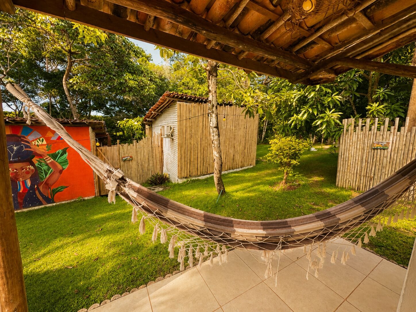 A hammock under a wooden pergola, a small shed, and a mural on a wall.