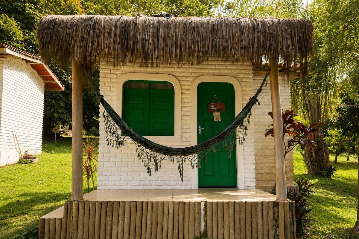 Una estructura de techo de paja con dos puertas verdes, una hamaca y una plataforma de madera.