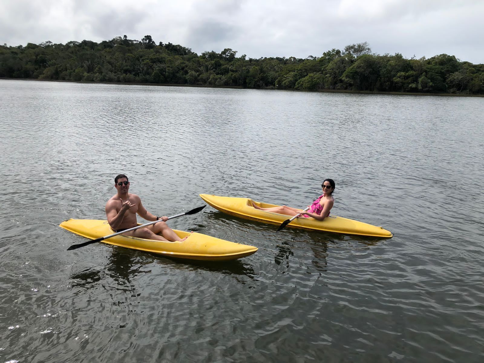 Two people kayaking on a calm lake with a forested shoreline in the background.