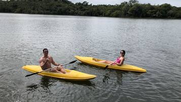 Two people kayaking on a calm lake with a forested shoreline in the background.