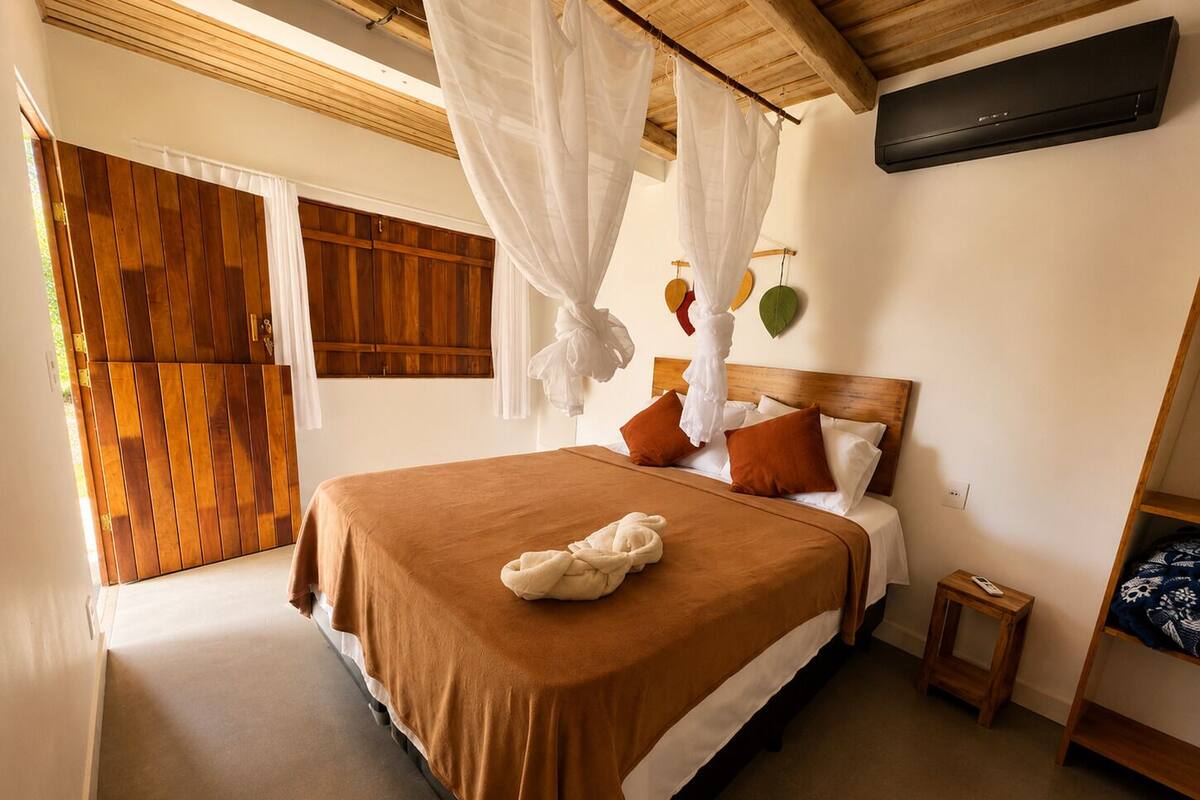 Un dormitorio con cama, mesita de noche, televisor montado en la pared y puerta de madera.