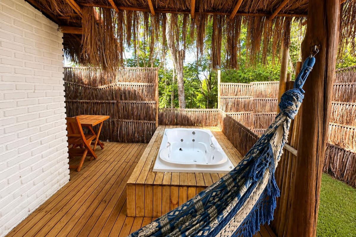 Una terraza de madera con un jacuzzi, una hamaca y una mesa.