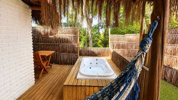 Una terraza de madera con un jacuzzi, una hamaca y una mesa.