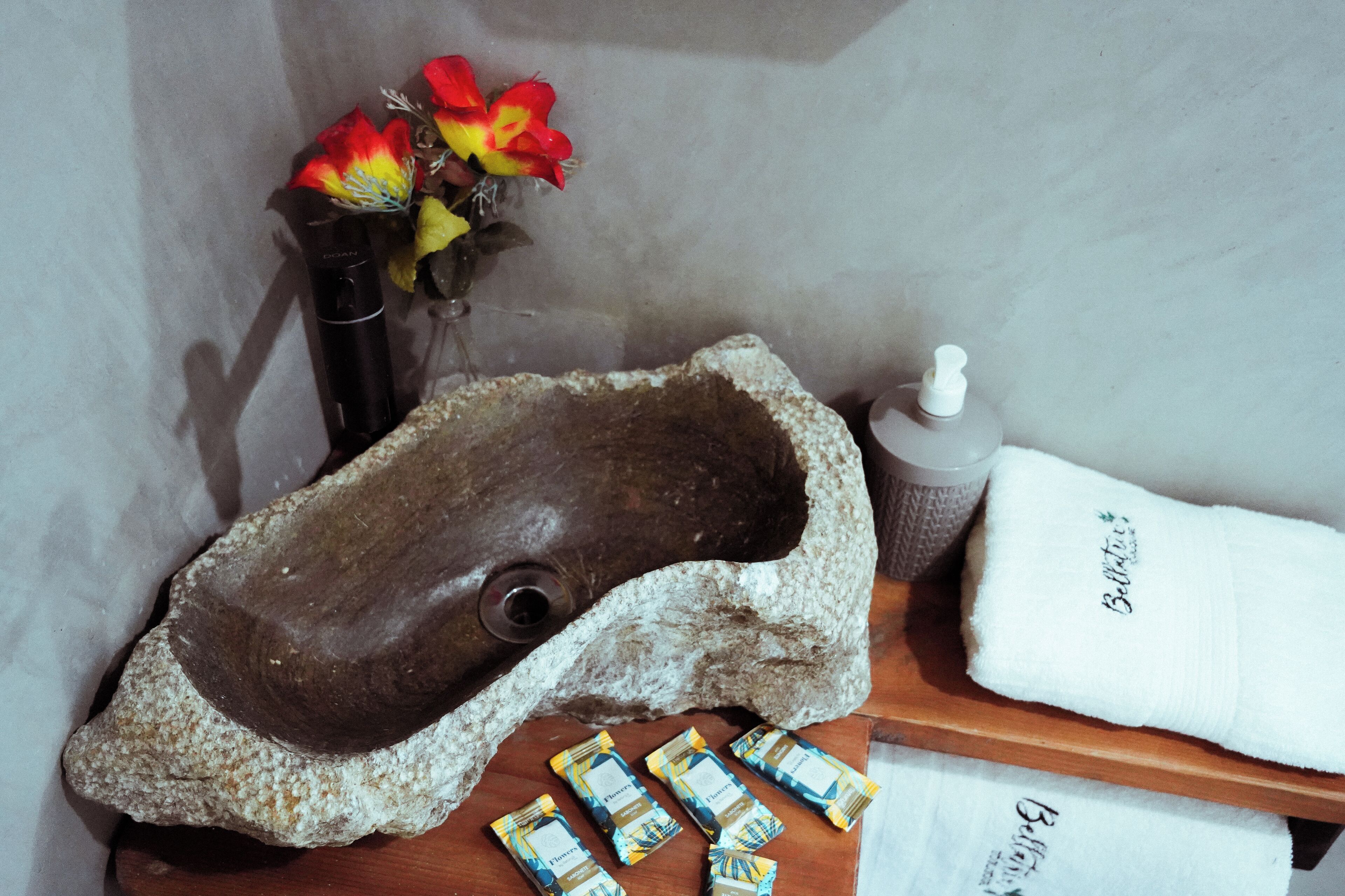 A stone sculpture, a bottle of lotion, a towel, and a vase with flowers on a wooden surface.