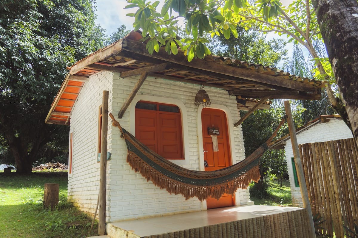 Una pequeña casa de ladrillo blanco con un porche de madera y una hamaca.