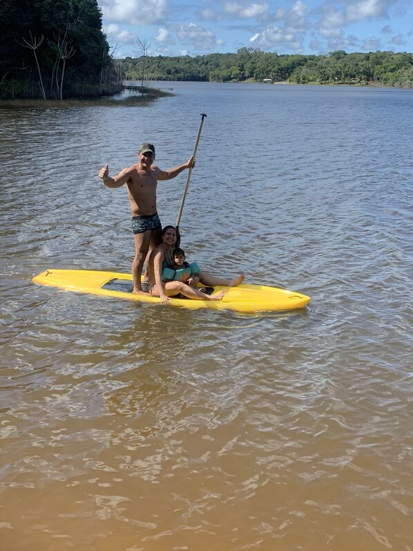 Een persoon staat op een geel paddleboard in het water, met een peddel in de hand.