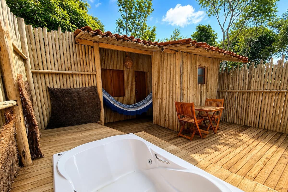 Una terraza de madera con un jacuzzi, una hamaca y una pequeña estructura de madera con un ventanal.