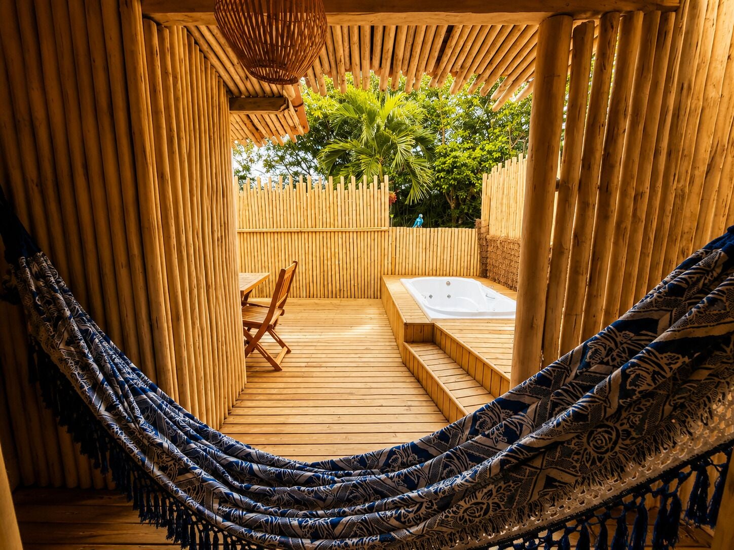 A hammock, wooden deck, and a hot tub in a bamboo enclosure.