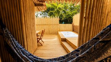 A hammock, wooden deck, and a hot tub in a bamboo enclosure.