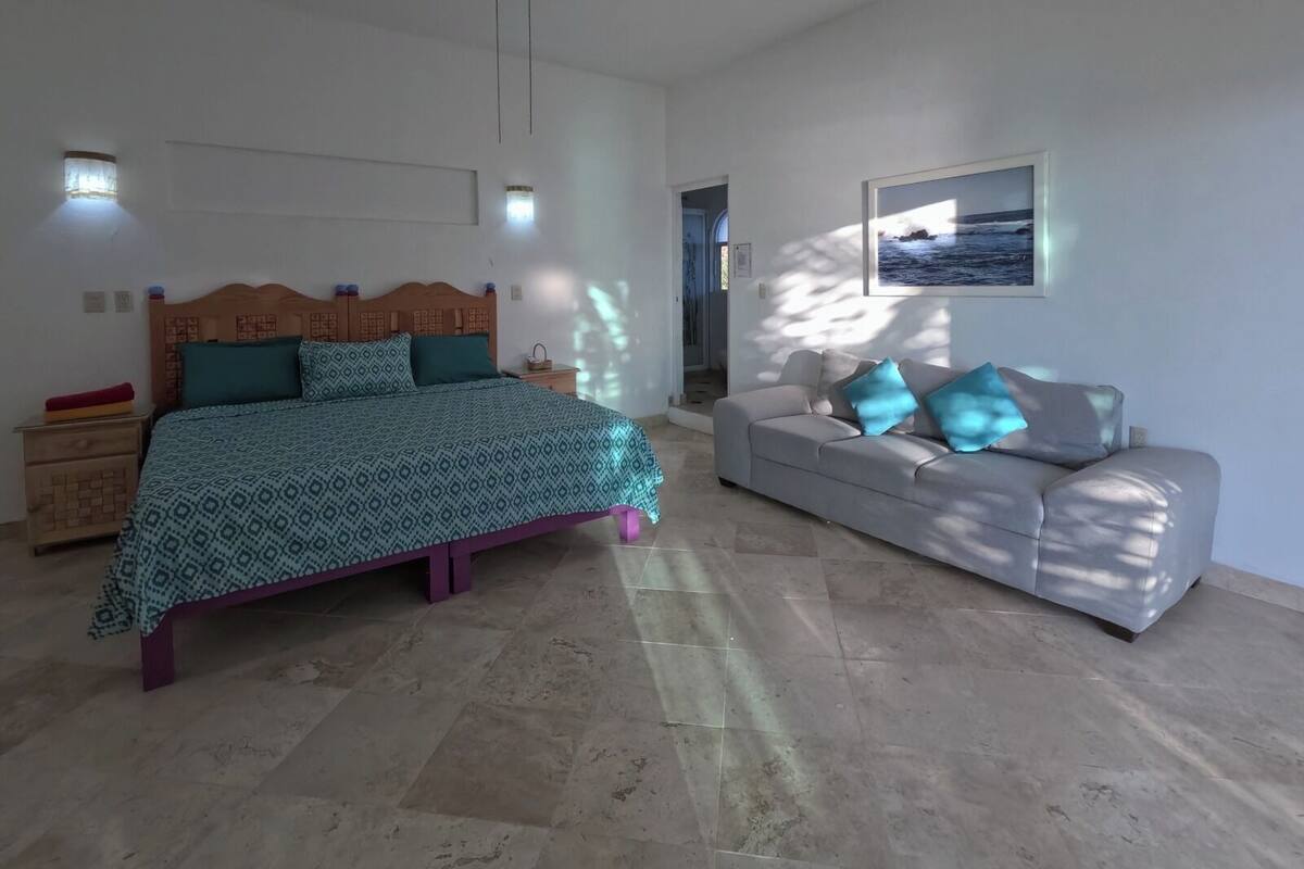 Un dormitorio con cama, ventilador de techo, sofá y un cuadro en la pared.
