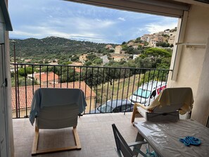 A balcony with a view of a hilly town, a white van, and a table with a blue object.