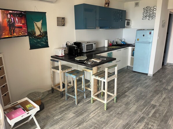 A compact kitchen with a central island, bar stools, a microwave, and a refrigerator. - CHARMING 30-square-meter STUDIO with a 15-square-meter TERRACE and an UNFORGETTABLE VIEW OF CALVI BAY (Lumio)