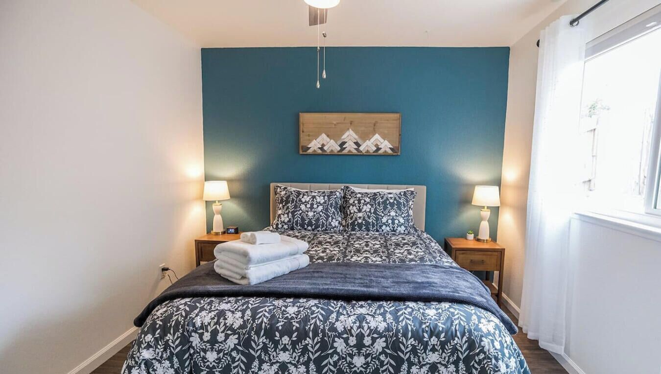 Quarto com uma cama, duas mesas de cabeceira com abajures, uma obra de arte na parede e uma janela com cortinas.