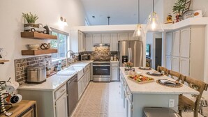 Une cuisine moderne dotée d’un îlot central, d’appareils électroménagers en acier inoxydable et de luminaires suspendus.