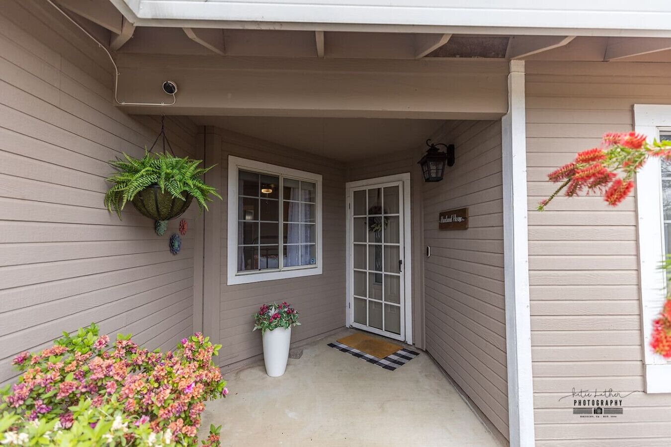 A house entrance with a covered porch, a potted plant, a window, a door, and a sign.