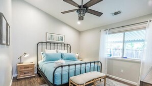 Un dormitorio con cama, mesita de noche, lámpara y ventana con cortinas.
