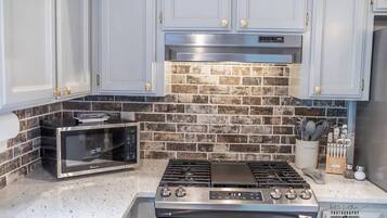A kitchen with a stainless steel stove, a microwave, and a brick backsplash.