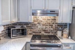 A kitchen with a stainless steel stove, a microwave, and a brick backsplash. - Hanland House | Home Away From Home (Redding)