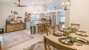 Une cuisine moderne dotée d’un îlot central, d’un coin repas avec une table en bois pour quatre personnes et d’un espace dédié à la préparation du café.