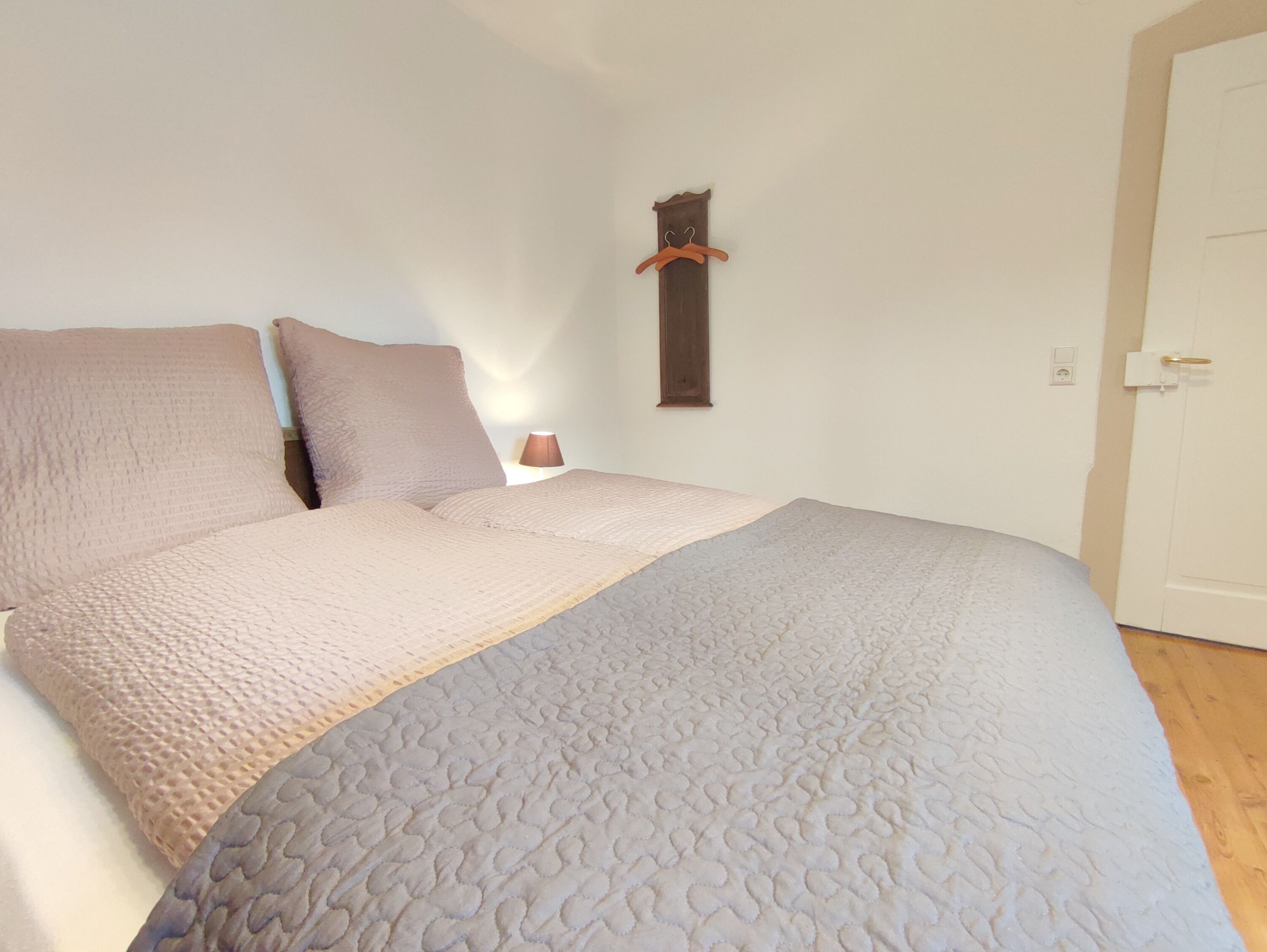 A bedroom with a bed, pillows, a bedside table, a lamp, and a coat rack.