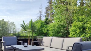 An outdoor seating area with a sofa, chairs, and a table, surrounded by greenery and trees.