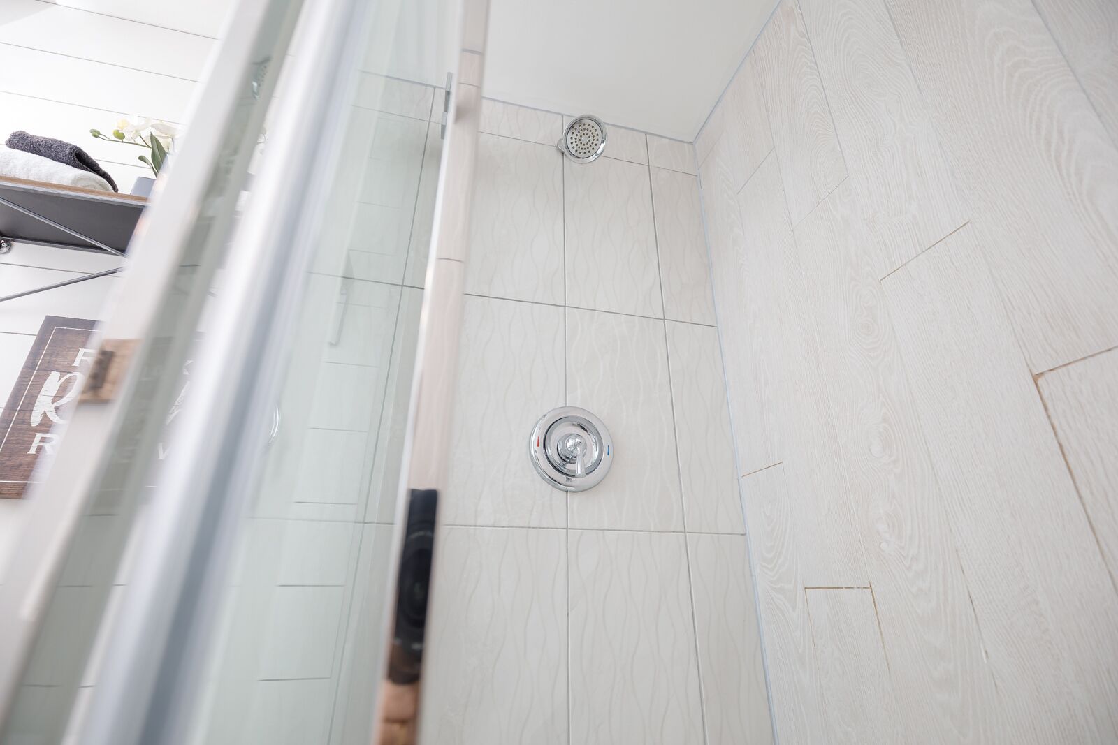 Une douche dotée d’un robinet chromé et d’un drain circulaire, de murs carrelés et d’une porte en verre.