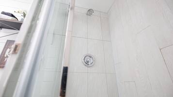 Une douche dotée d’un robinet chromé et d’un drain circulaire, de murs carrelés et d’une porte en verre.